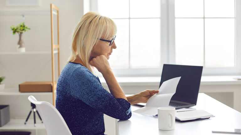 Kobieta czytająca dokumenty przy laptopie